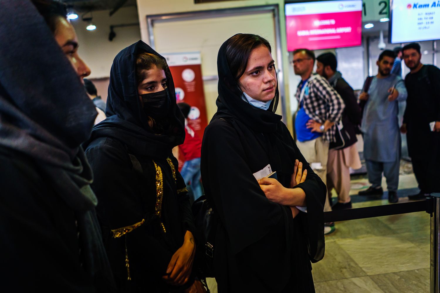 Young women in headscarves wait at an airport boarding gate.