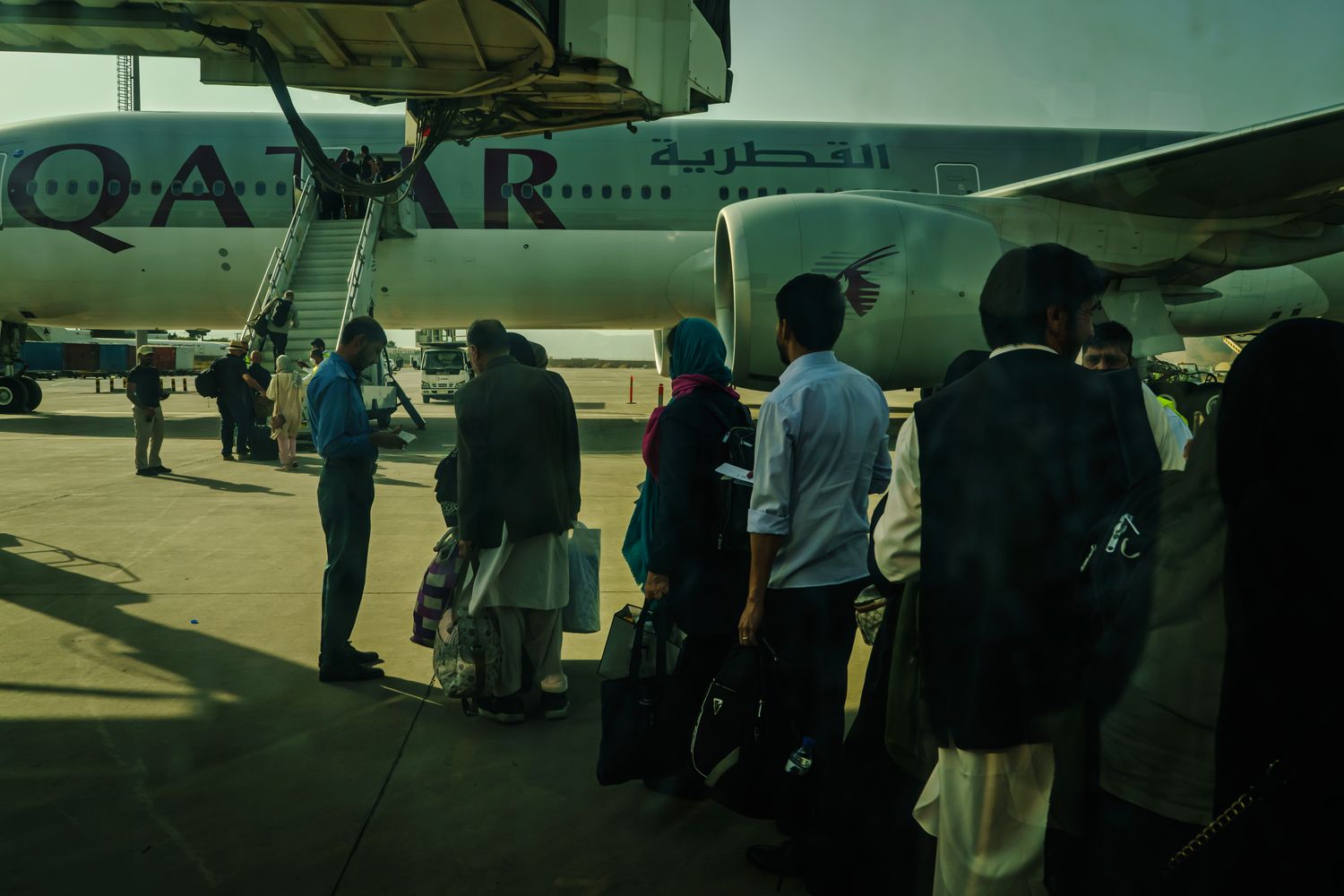 A line of passengers waits on a tarmac to board a Qatar Airways plane.