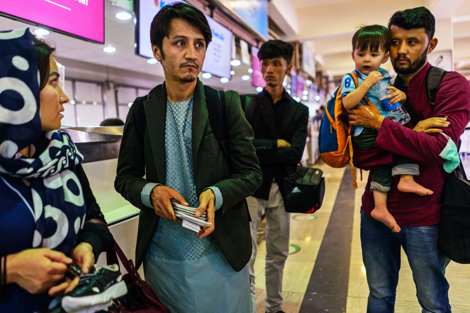 A man holding passports stands next to family members near an airport check-in counter.