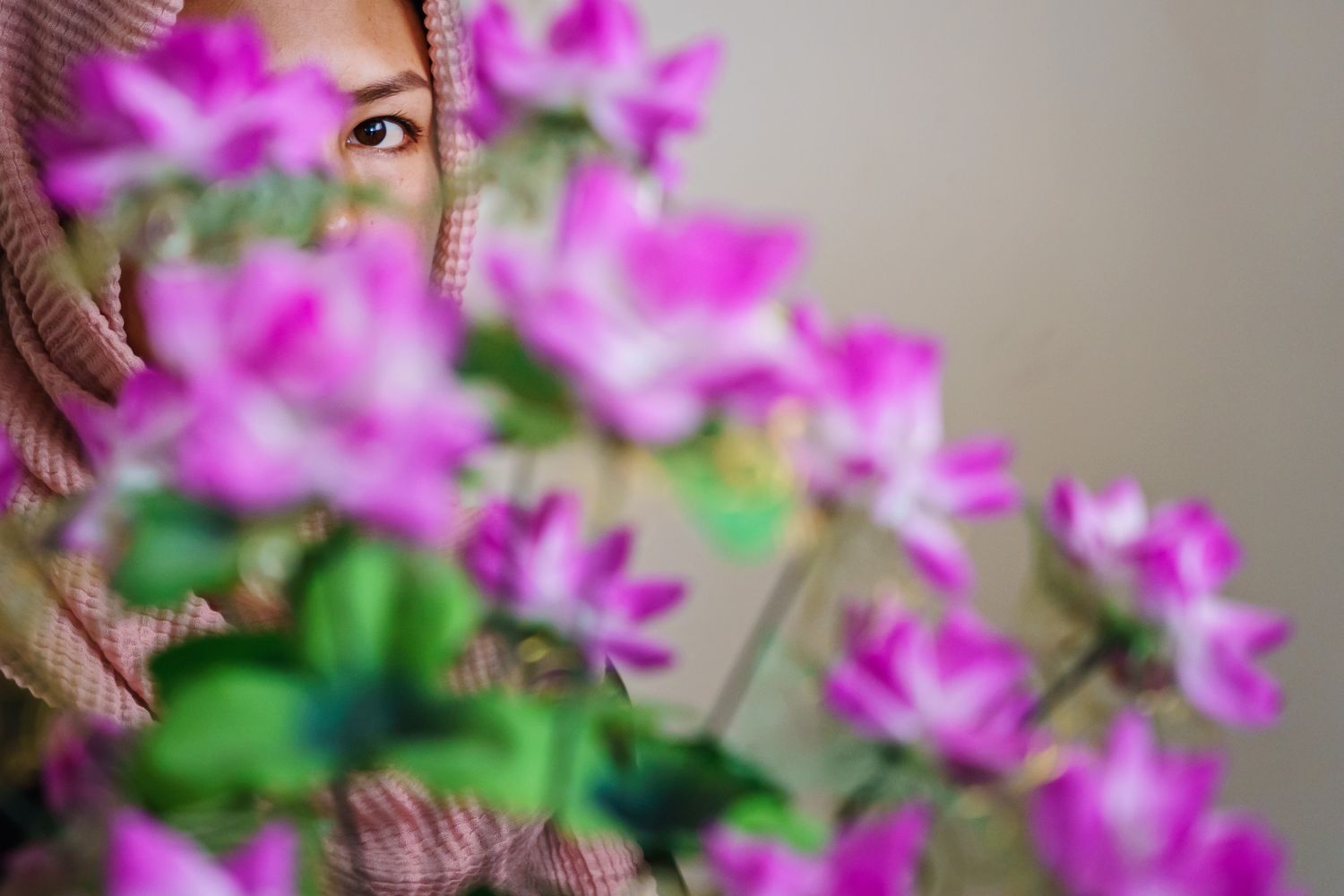 The eye of a woman in a head scarf peeks through a bouquet of pink flowers.