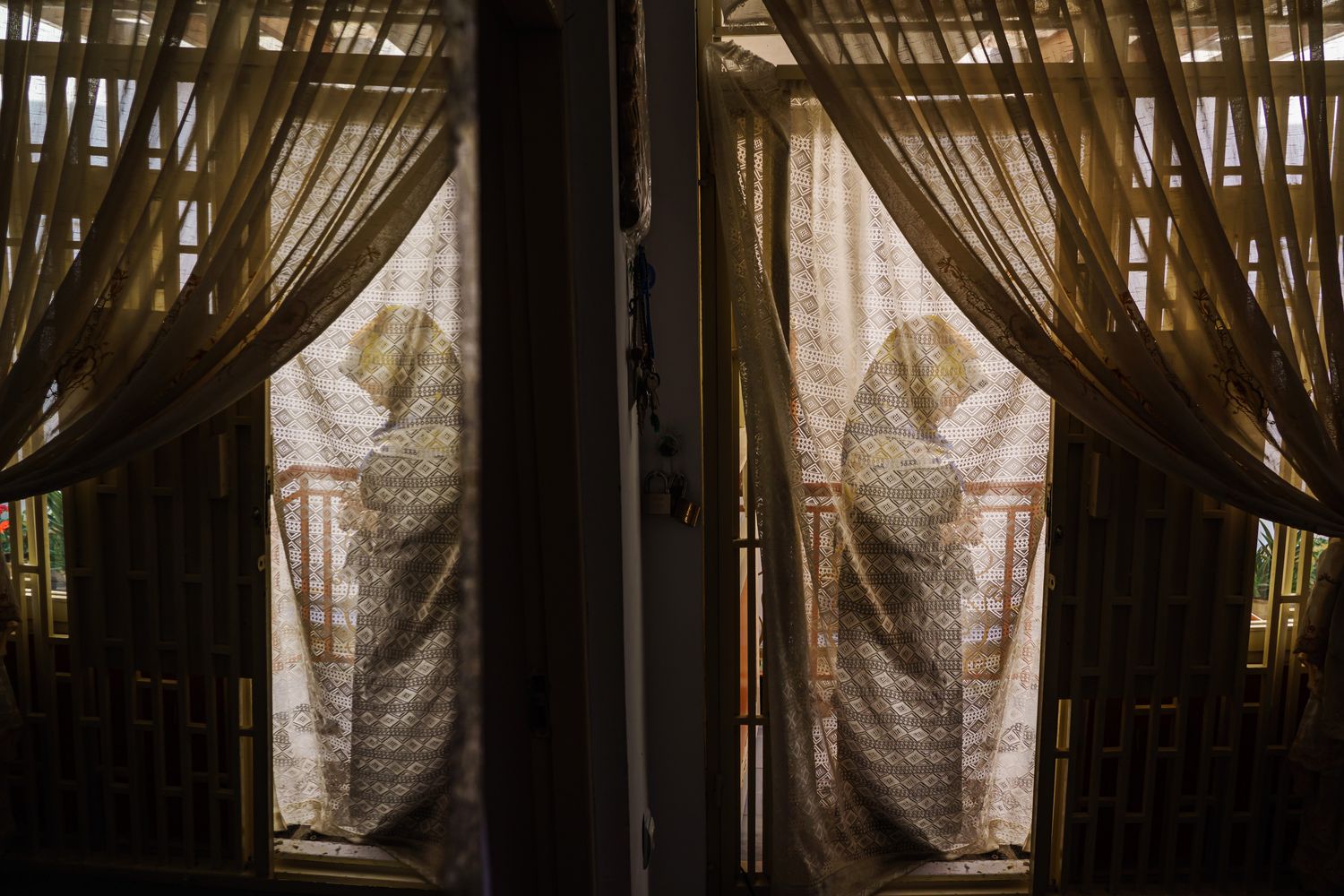 A woman silhouetted against the drapery of a doorway.