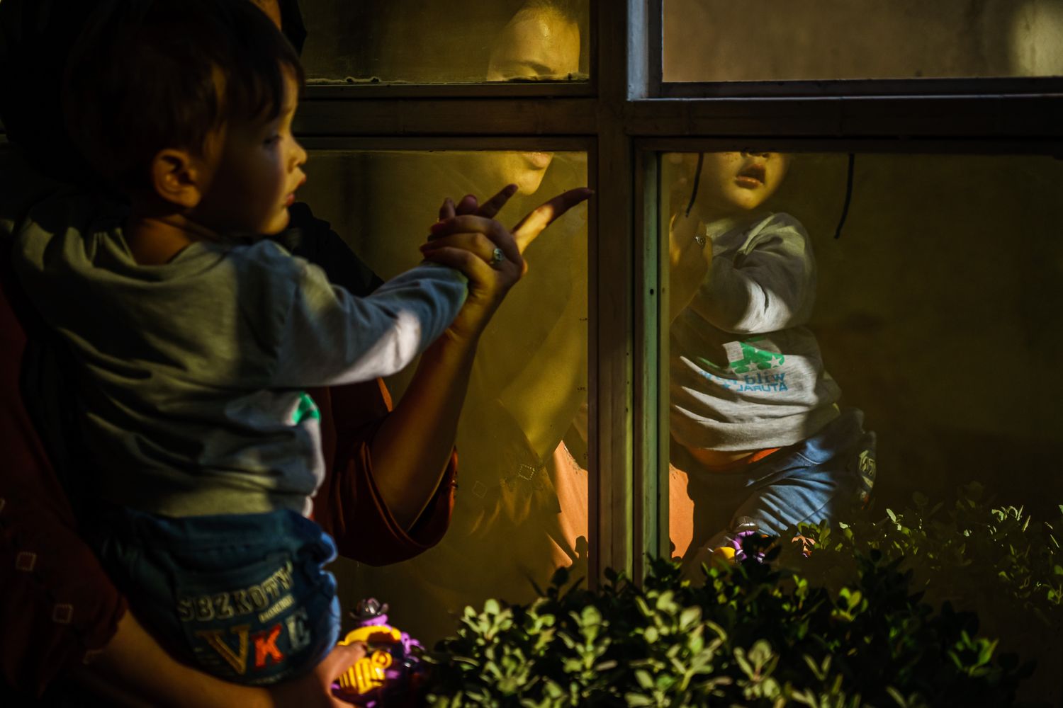 A woman holding a toddler is reflected in the glass of a window.