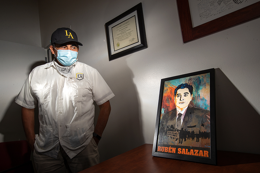 Robert Lopez, Executive Director for Communications and Public Affairs at Cal State University Los Angeles and a former Los Angeles Times reporter, stands next to a framed poster of Ruben Salazar