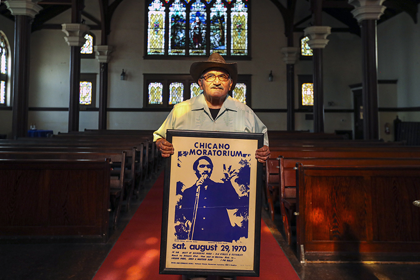 Rosalío Muñoz holds a framed poster of the Aug. 29, 1970 Chicano Moratorium.