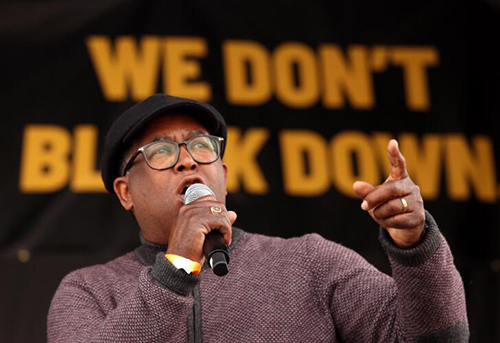 Mark Ridley-Thomas holds a microphone with one hand and points up with the other.