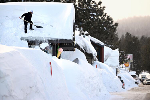 A man shovels snow off a roof and onto a tall snowbank. 