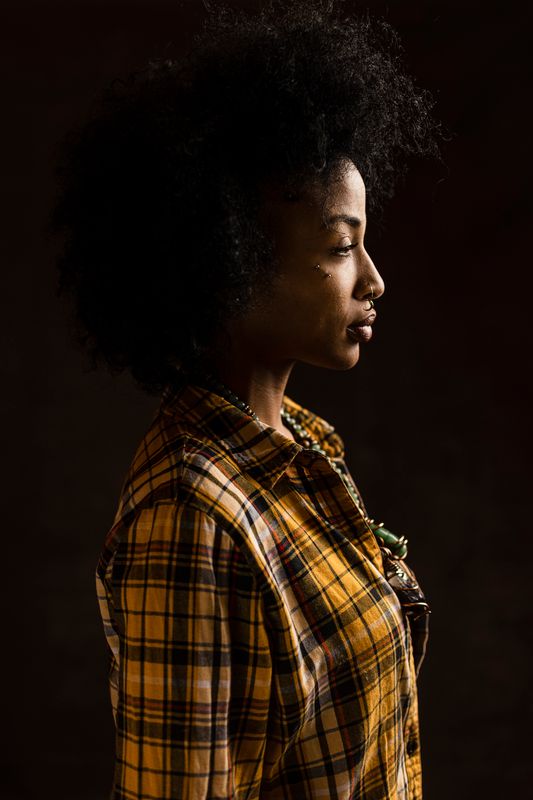 Corrie DeCosta stands in profile wearing a flannel