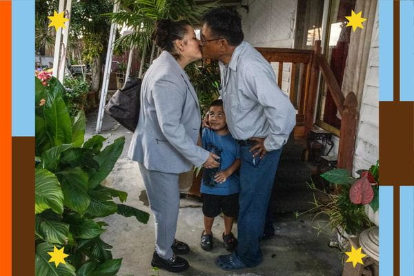 A woman and man kiss in front of their mobile home, their child in between them.