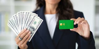 A woman holding a credit card in one hand and cash in the other.