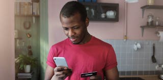 Young african american man holds smartphone in one hand, checking his credit score