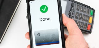 A phone showing a mobile wallet with a credit card completing a transaction above a card machine. 